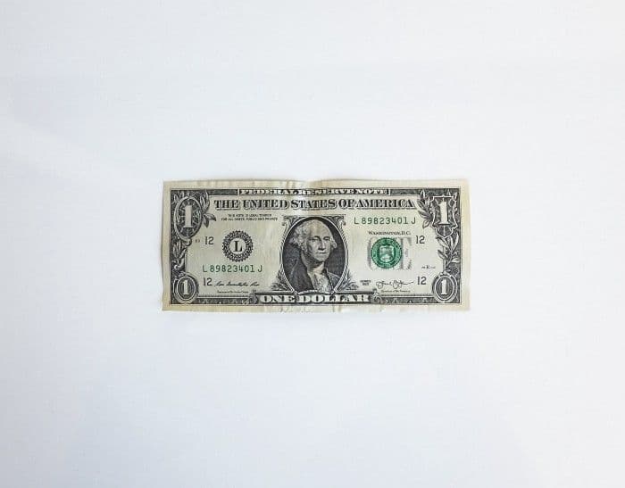 A single creased one dollar bill lying flat on a plain white surface.