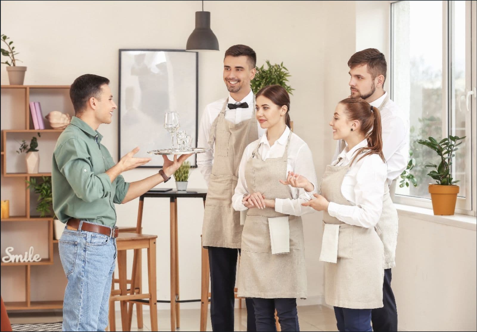 A restaurant manager talking with five servers in aprons and white shirts during a staff training session.