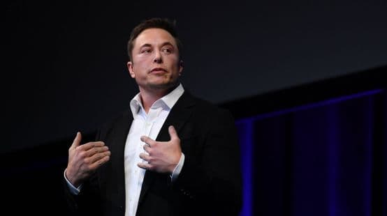 A business leader in a dark blazer speaking on stage with hands raised mid-gesture