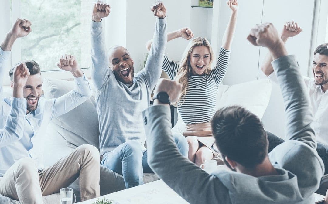 A group of coworkers on a couch cheering with raised fists, celebrating a win for their business.