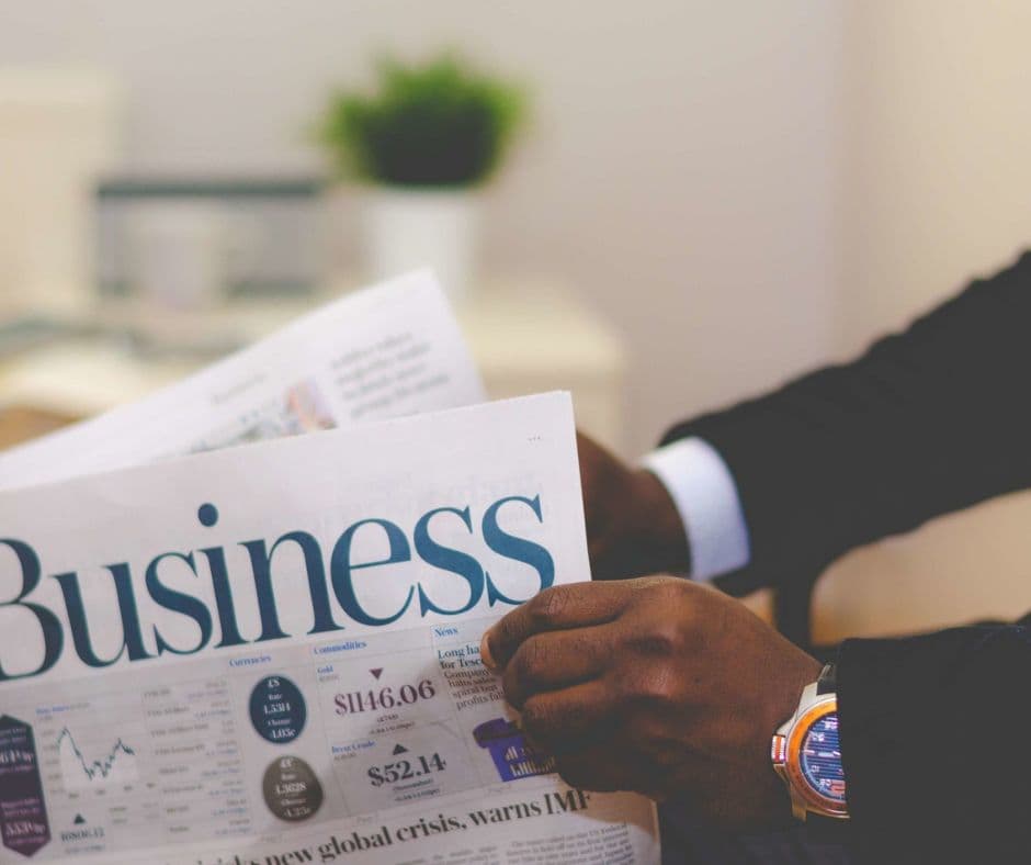 Person in a suit reading a business newspaper with stock market figures and a global crisis headline