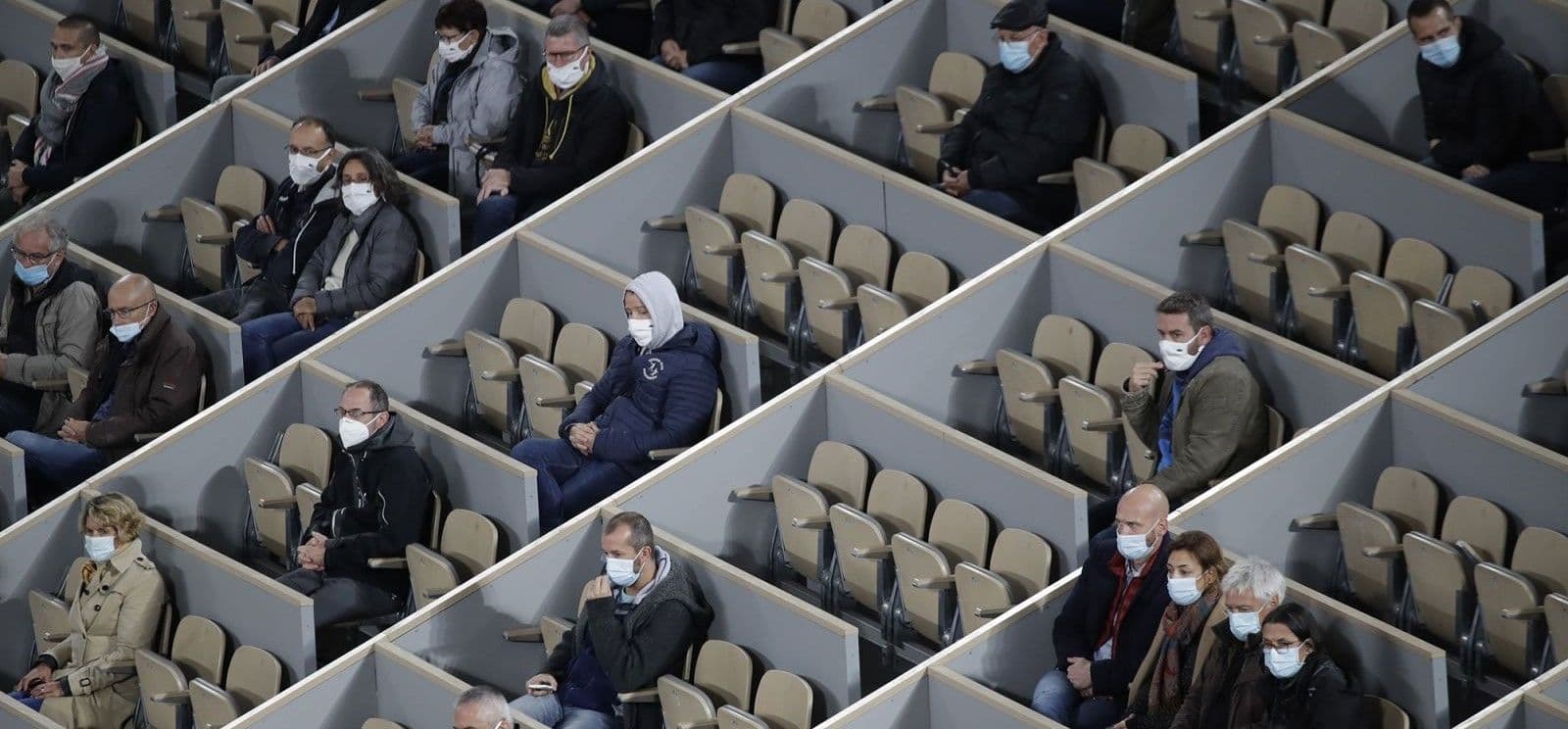 Spectators wearing face masks sit spaced apart in partitioned arena seating during the pandemic