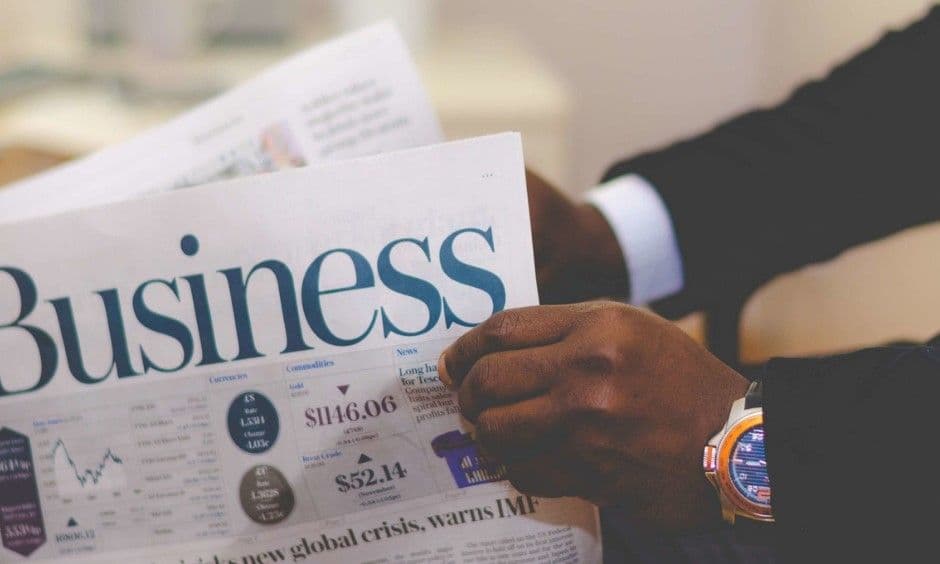 Person in a suit reading a business newspaper with stock market figures and a global crisis headline