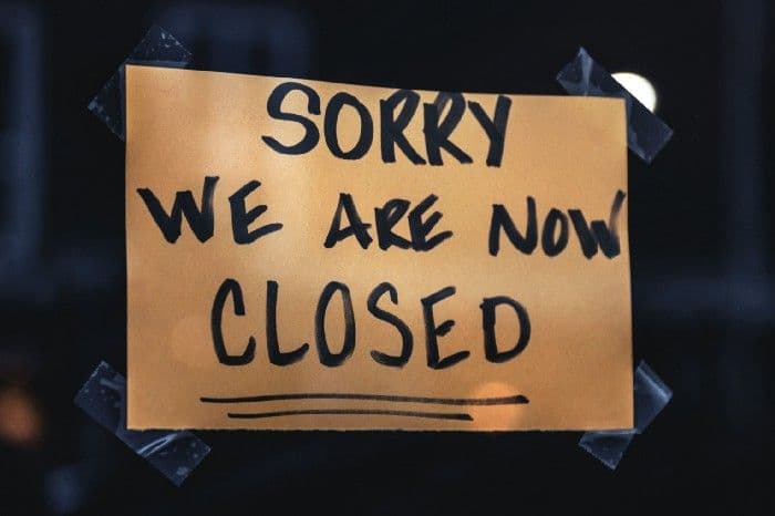 A handwritten sign taped to a darkened shop window reading Sorry we are now closed.