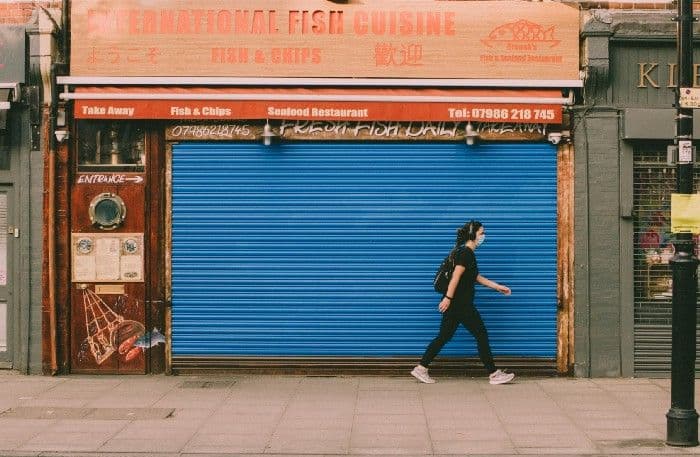 A masked pedestrian walks past a takeaway restaurant with its blue metal shutter pulled down.