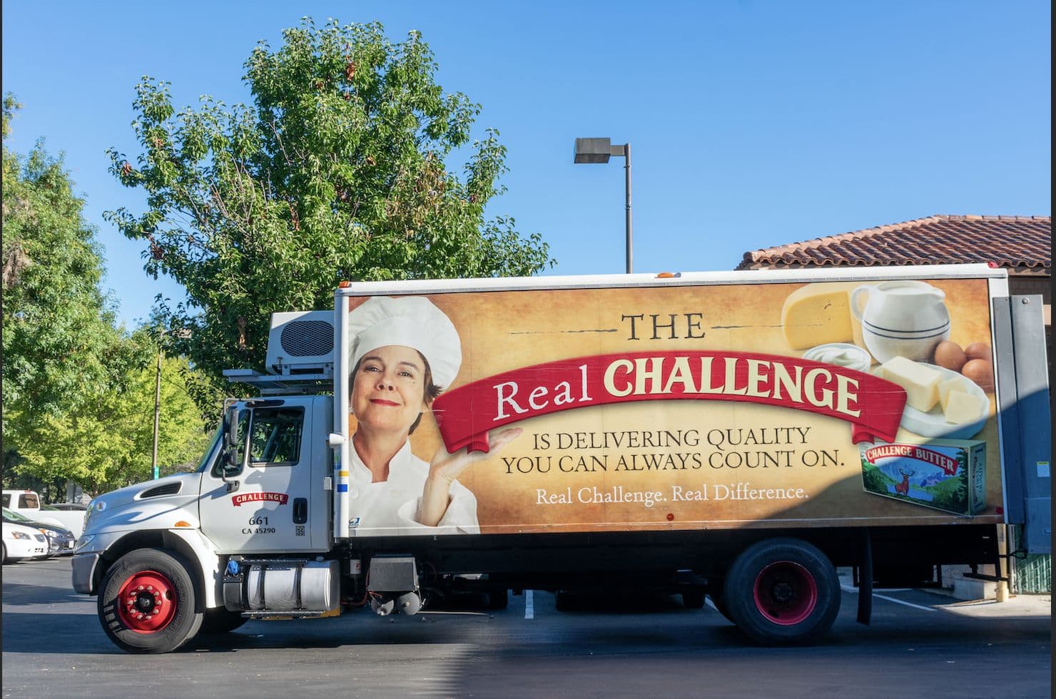 A box delivery truck in a parking lot with a large side ad reading "The Real Challenge is delivering quality you can always count on."