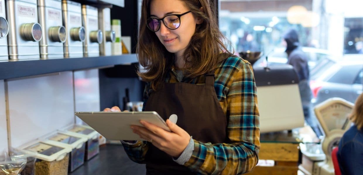 A coffee shop employee using a tablet behind the counter.