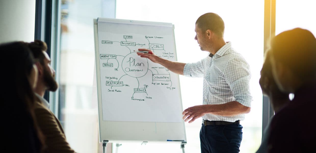 A person presenting a planning diagram on a flip chart to two colleagues in an office.