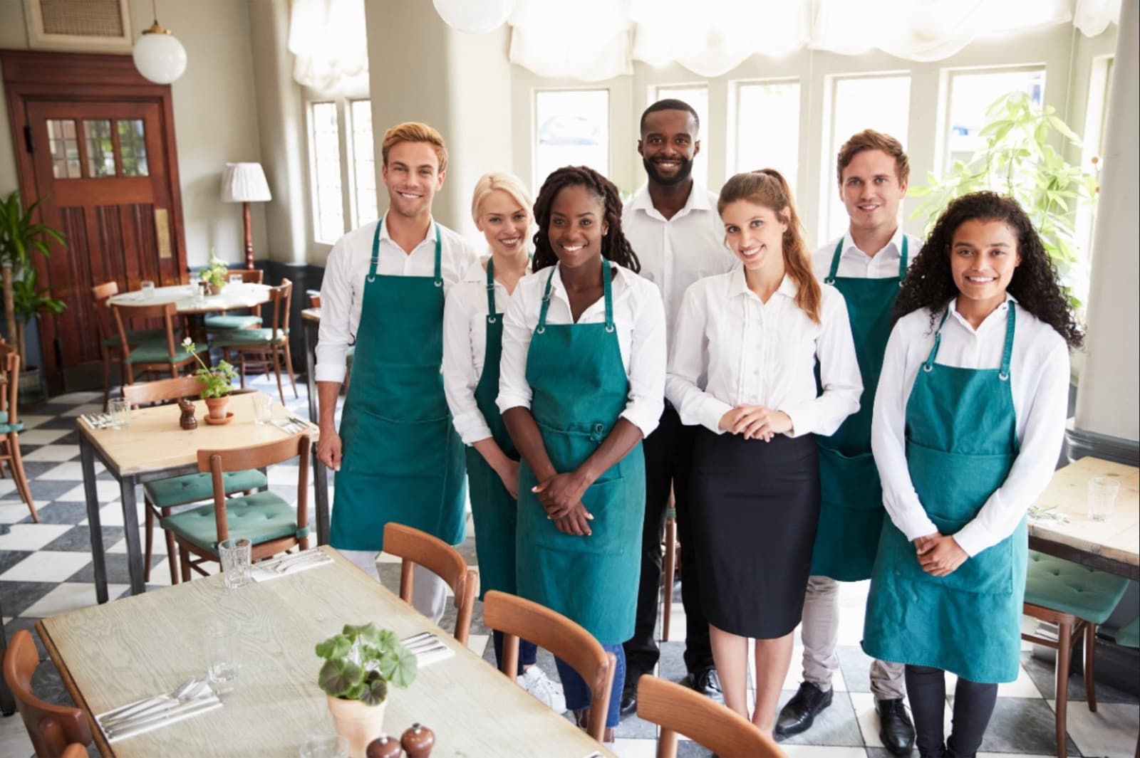 A restaurant team in clean aprons and uniforms standing together in a dining room.