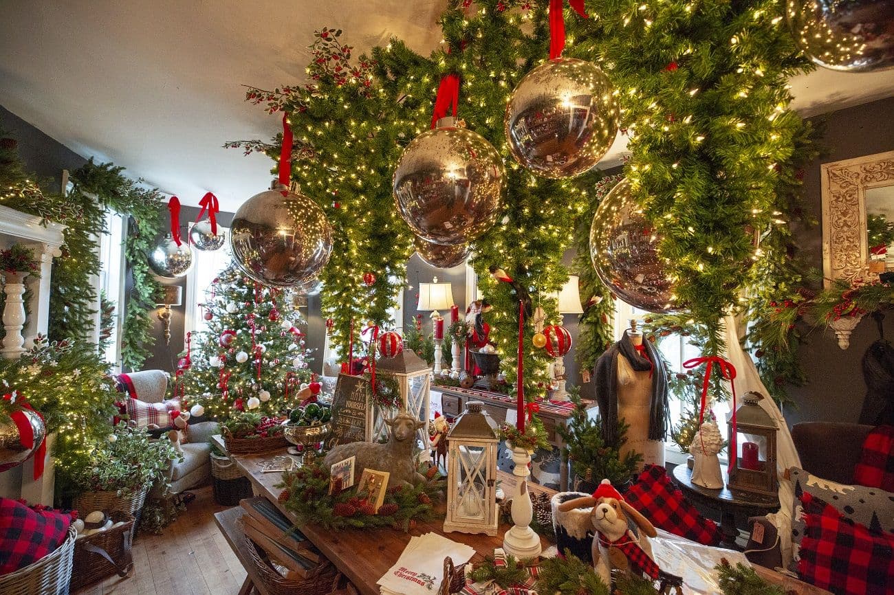 A retail interior dressed for the holidays with garlands, lit Christmas trees, oversized silver ornaments, and red ribbons.