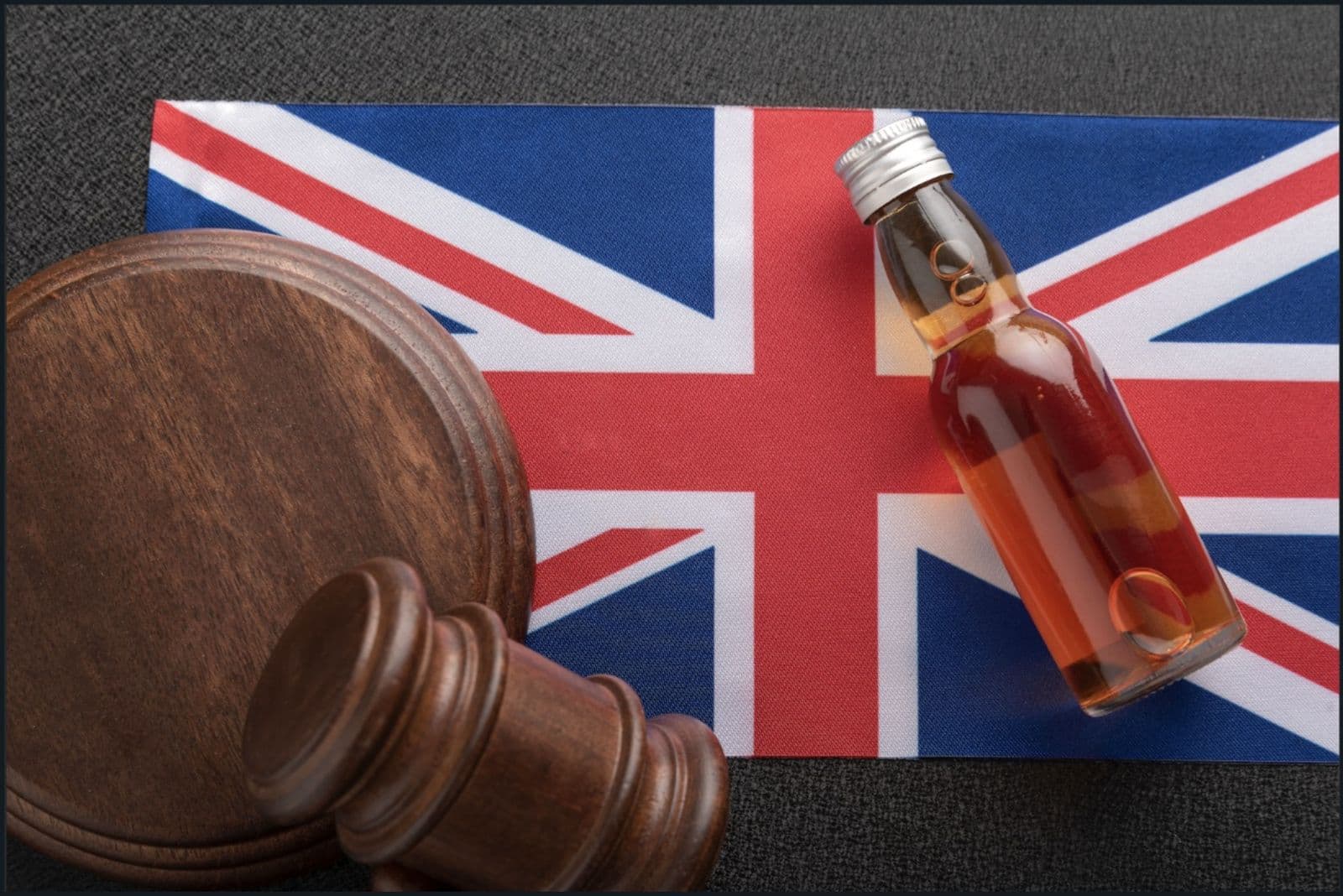 A wooden judge's gavel and a small bottle of amber liquor resting on a British flag.