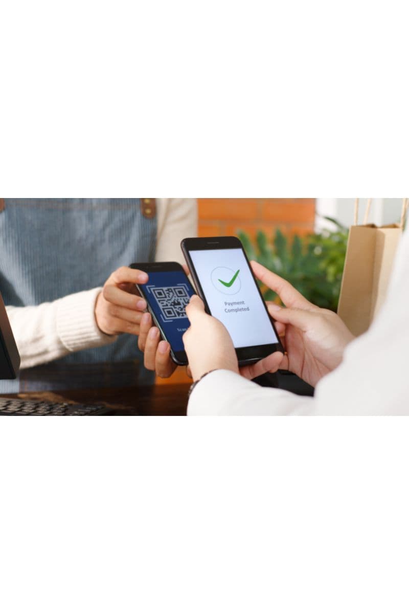 Two people complete a contactless QR code payment between smartphones at a restaurant counter, with a 'Payment Completed' confirmation on screen.