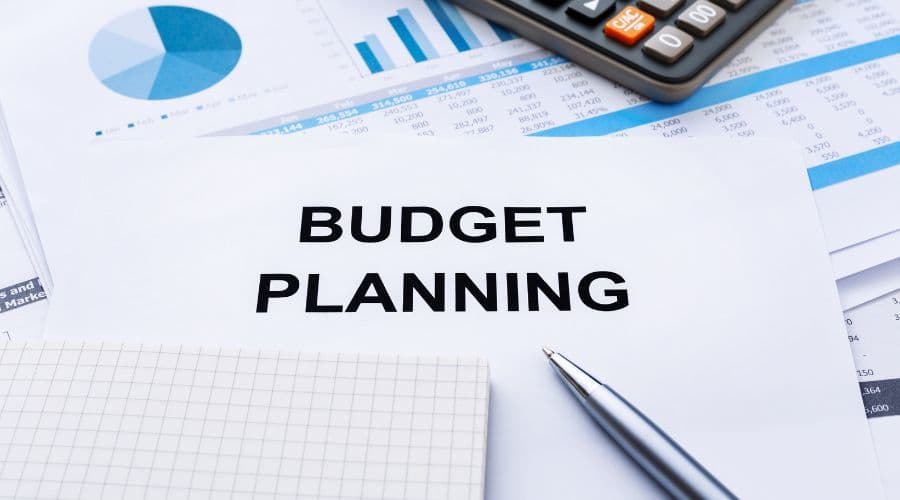 A printed sheet reading Budget Planning on a desk with financial charts, a calculator, a notepad, and a pen.