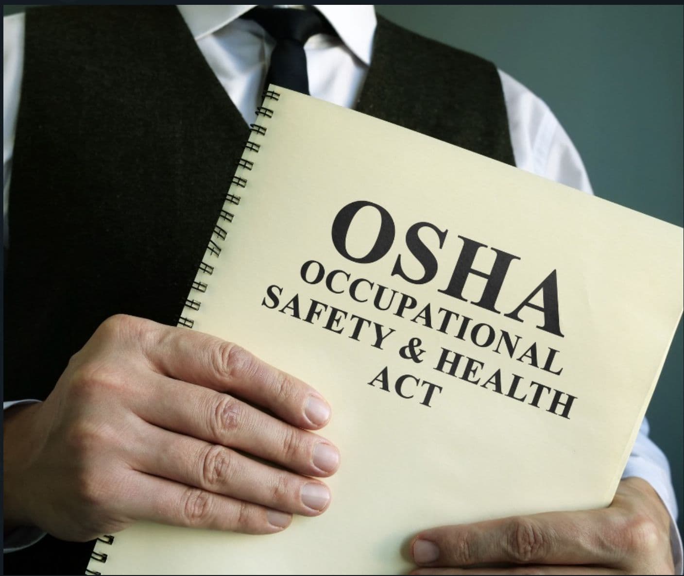 A person in a vest and tie holding a spiral notebook labeled OSHA Occupational Safety and Health Act.