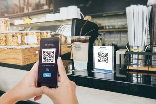 A customer scanning a QR code on a cafe counter with a smartphone to view the menu and pay.