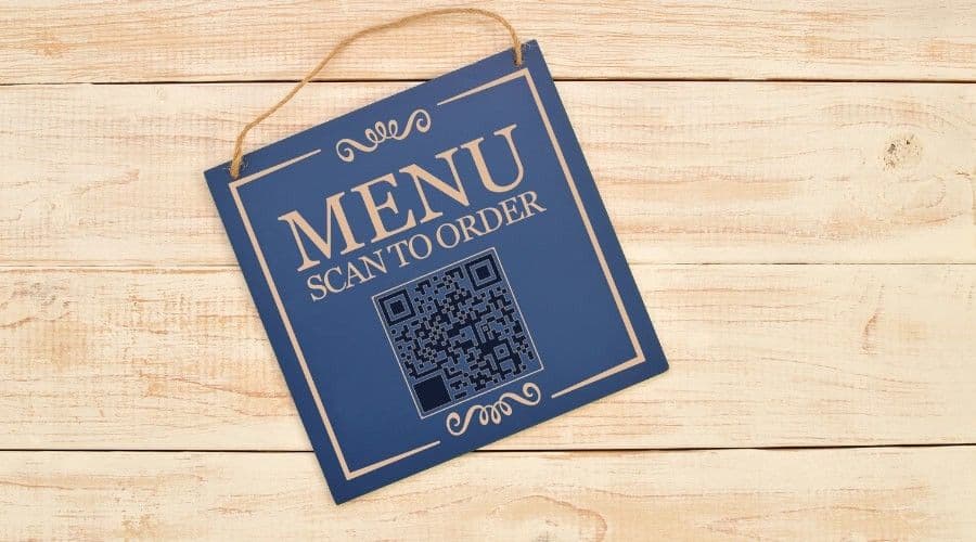 A wooden 'Menu: Scan to Order' sign with a QR code hanging on a wood-paneled wall.