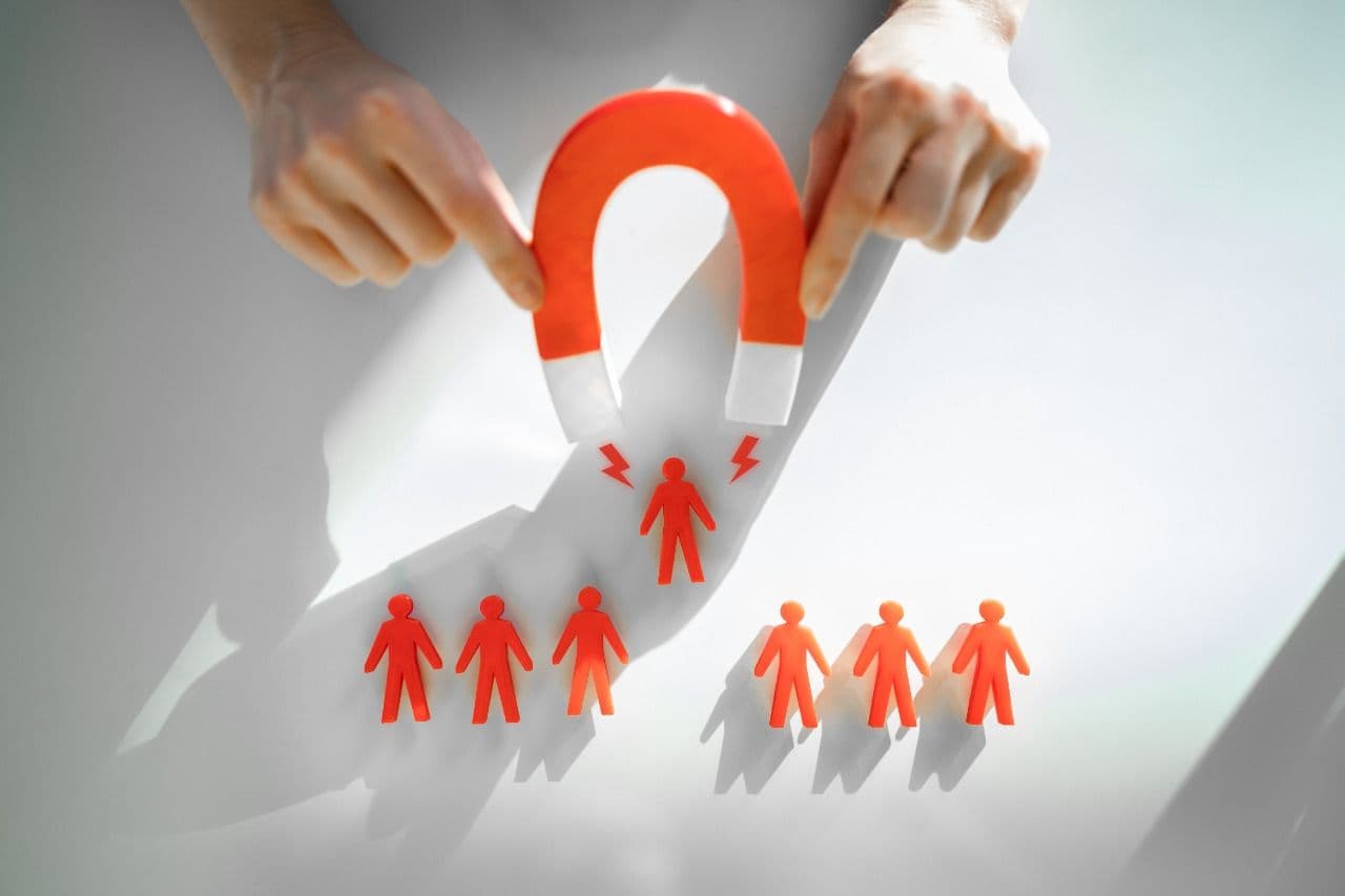 A red horseshoe magnet attracting one paper cutout figure away from a group, illustrating attracting and retaining talent.