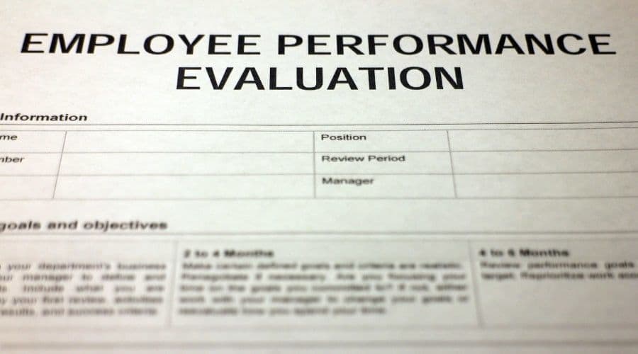 A printed Employee Performance Evaluation form with sections for name, position, review period, manager, goals, and objectives.