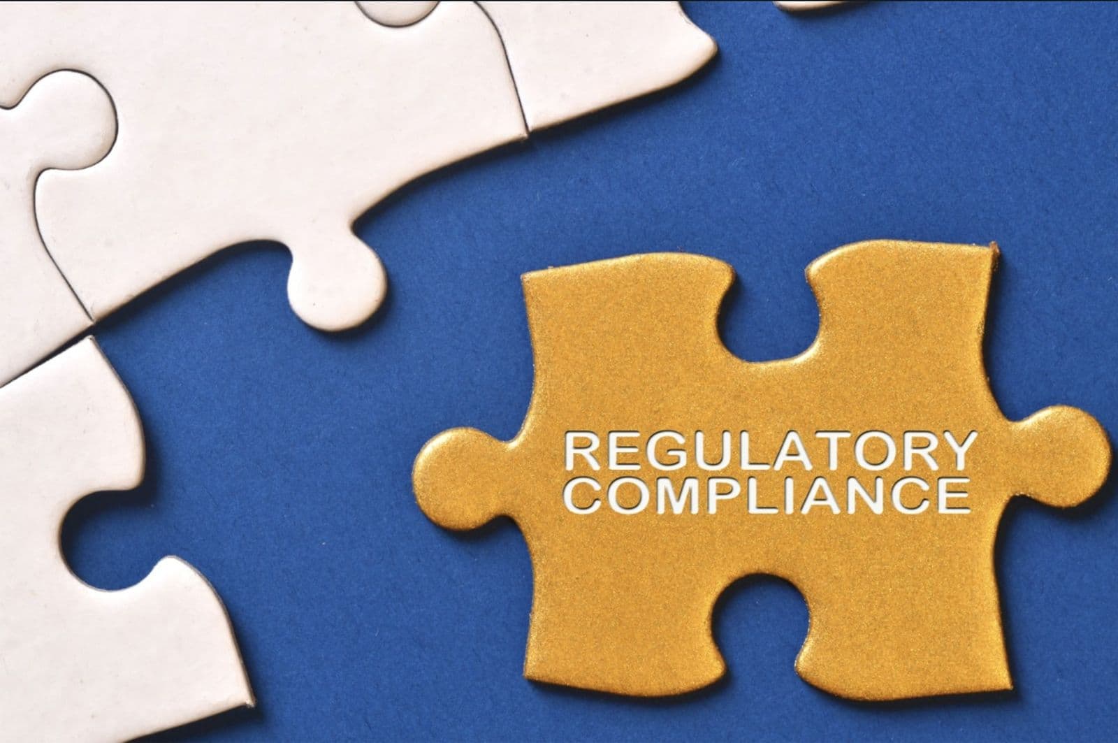 A golden puzzle piece labeled Regulatory Compliance set against a blue background next to white puzzle pieces.