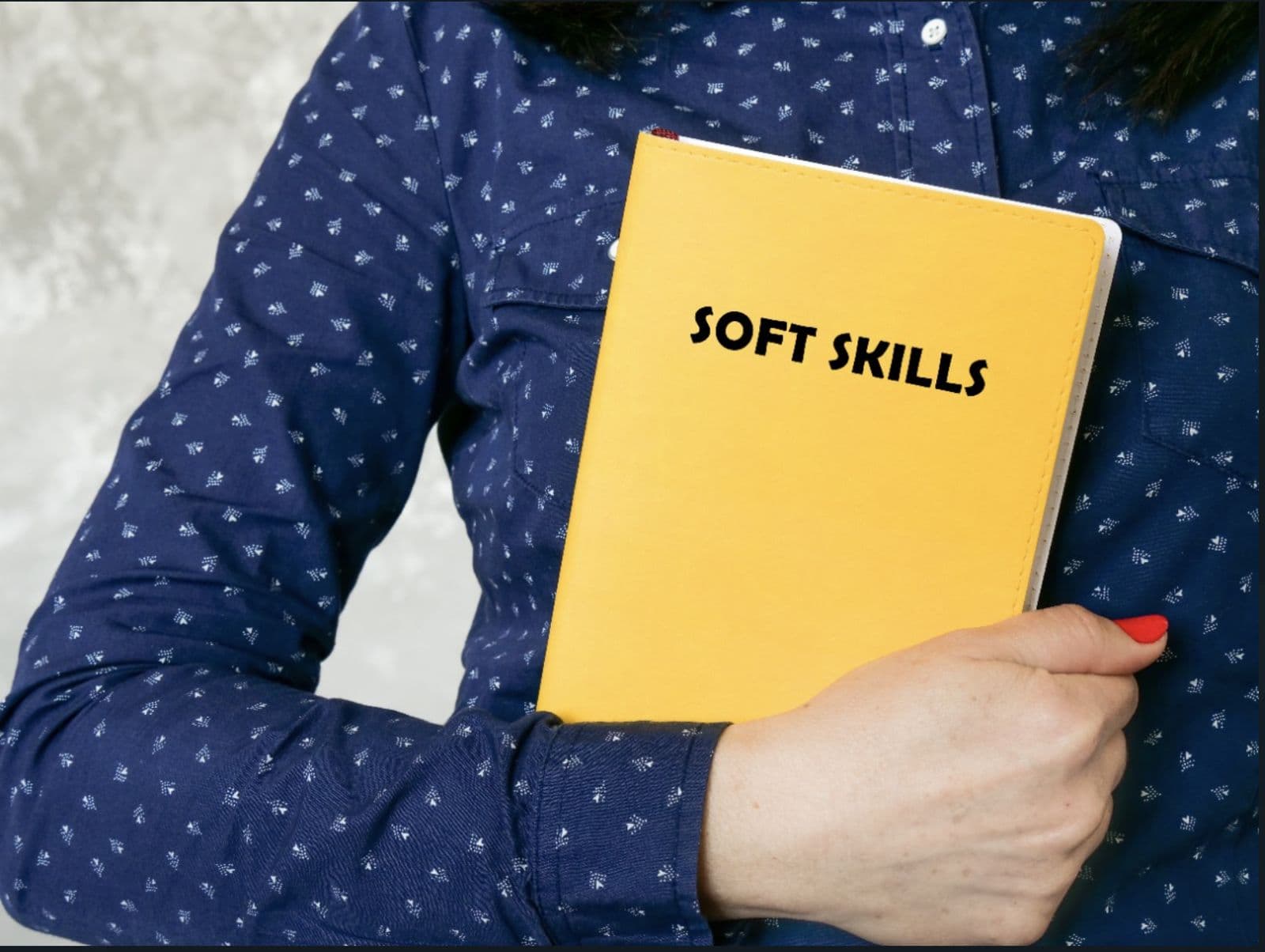 A person in a blue shirt holding a bright yellow notebook labeled Soft Skills.