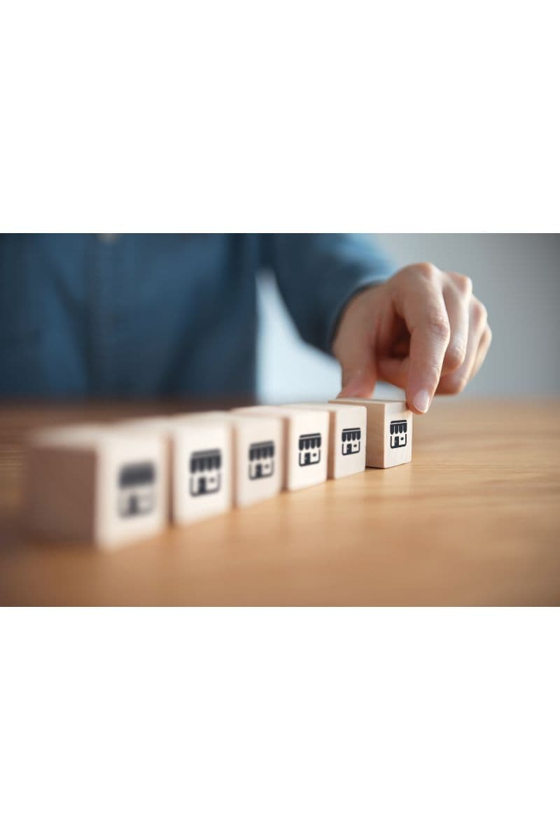 A hand lining up wooden blocks marked with storefront icons in a row, representing multiple franchise locations.
