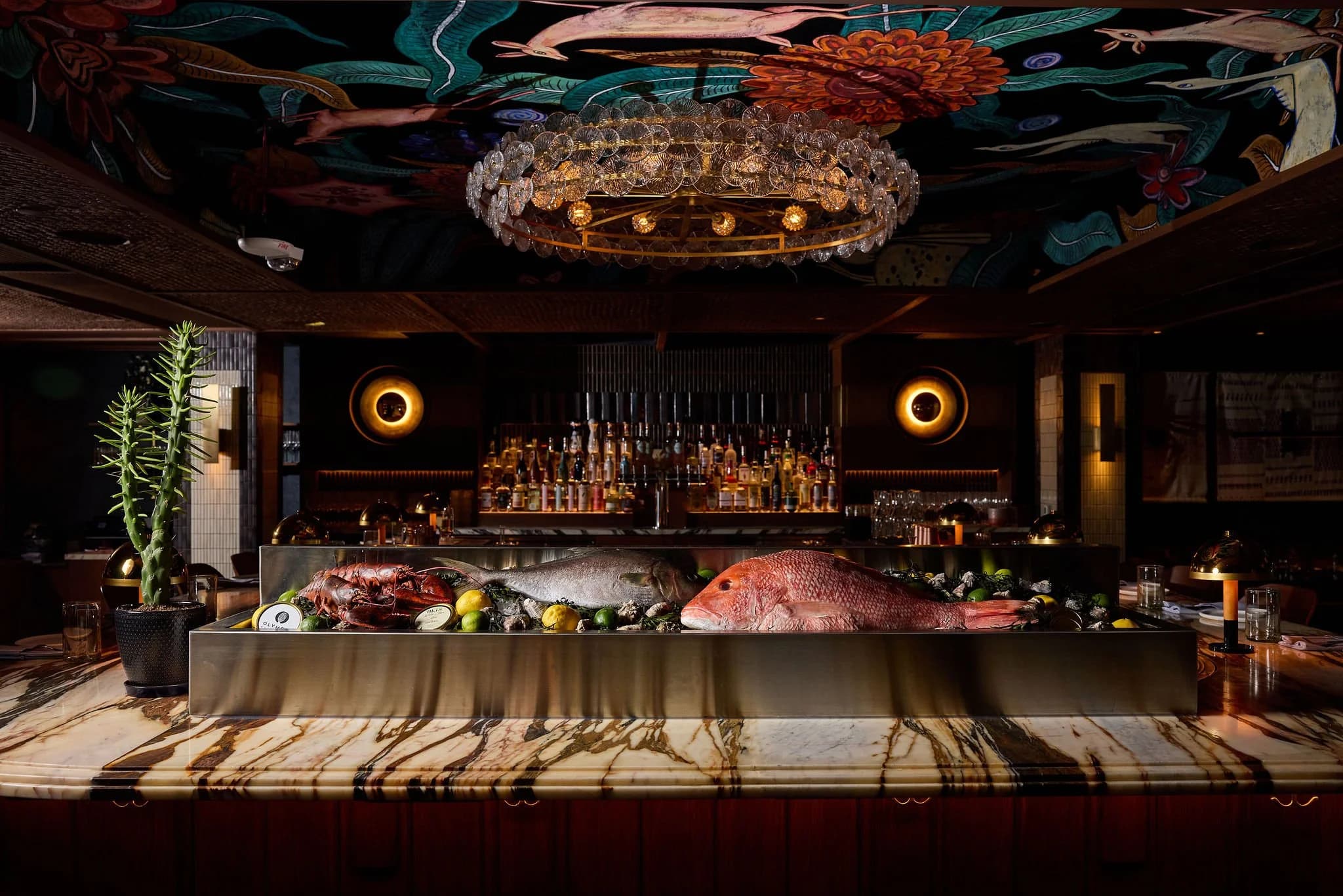 The dining room and bar at Alteño in Denver, with a chandelier and a seafood display on the marble bar