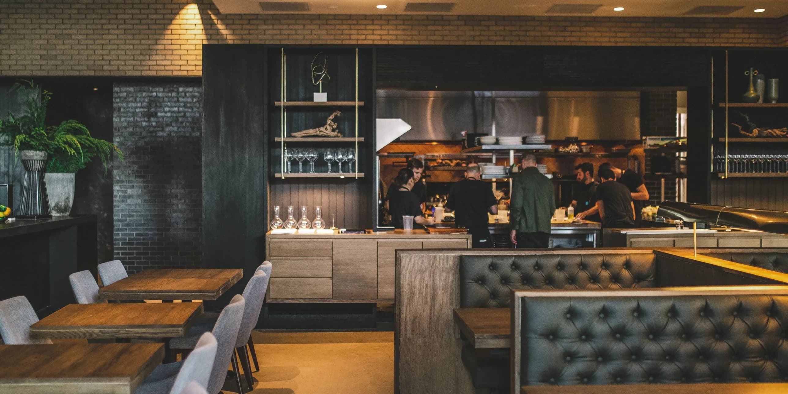 The dining room at Hestia in Austin, with leather booths, wood tables, and the open kitchen behind them